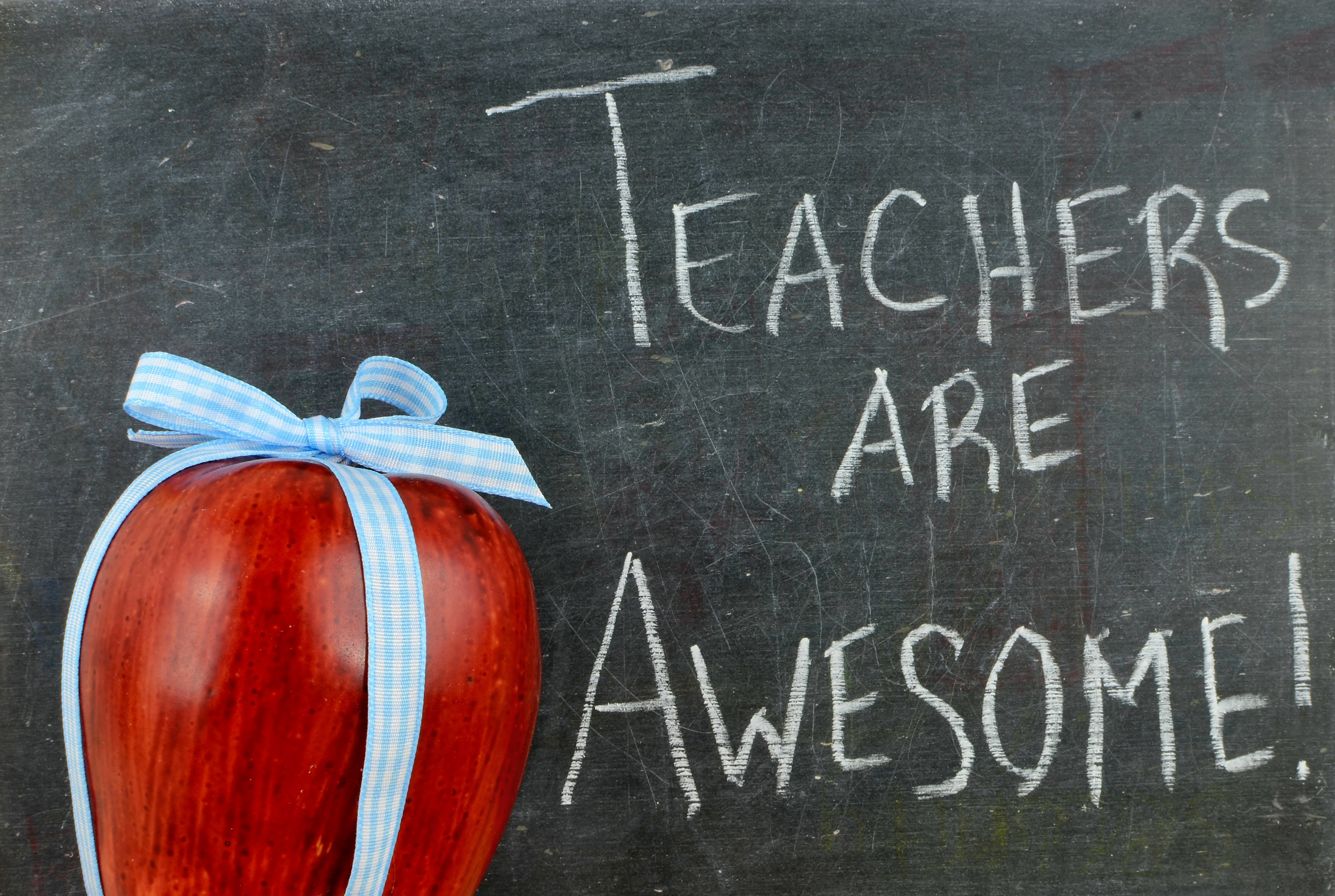 Chalkboard message stating “Teachers are awesome!“ with a red apple wrapped in a blue plaid ribbon.