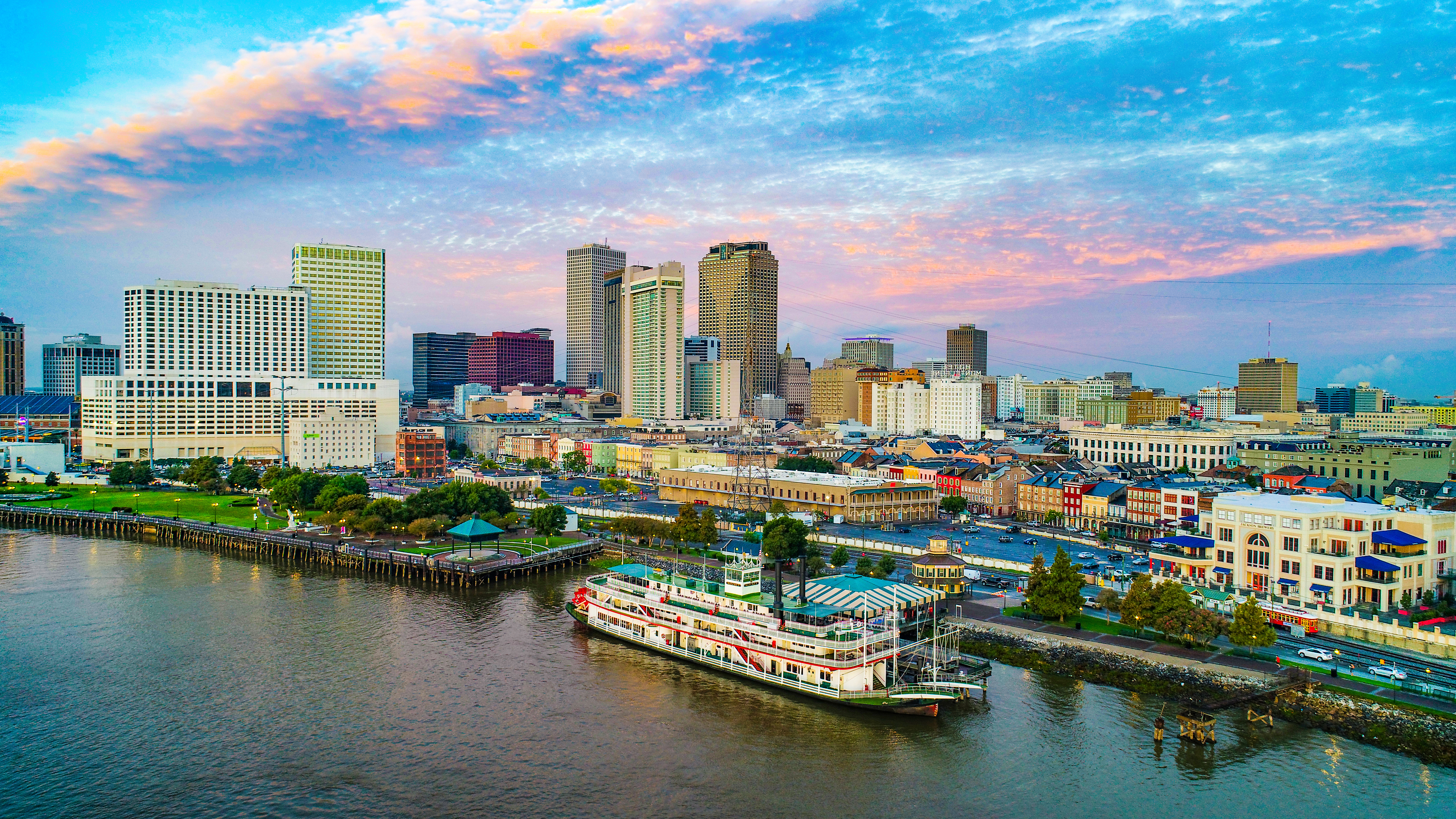 Image of New Orleans in front of a sunset, with a boat on the water in the forefront.