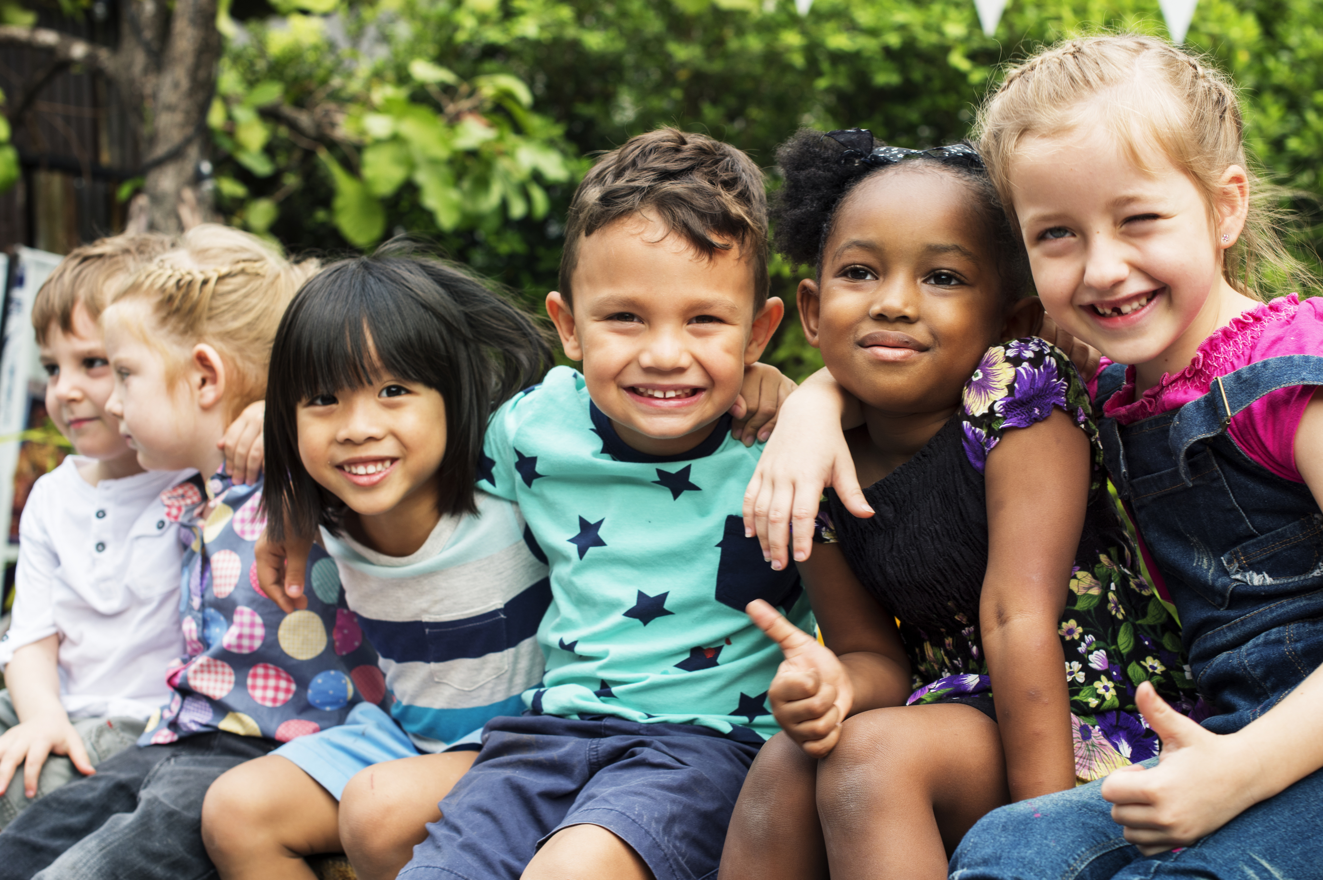 A group of children sitting and smiling outside.