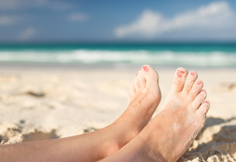 Bare feet on a sandy beach with painted toenails. 