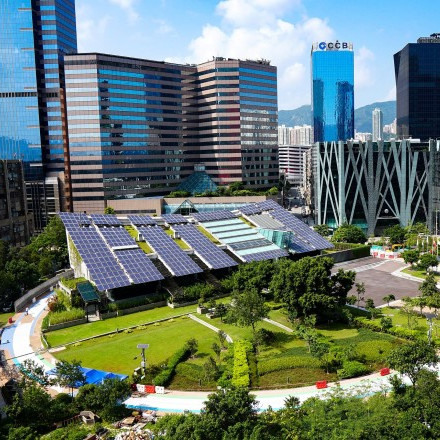 photo of a large solar panelled roof building in a park surrounded by glass sky-scrapers