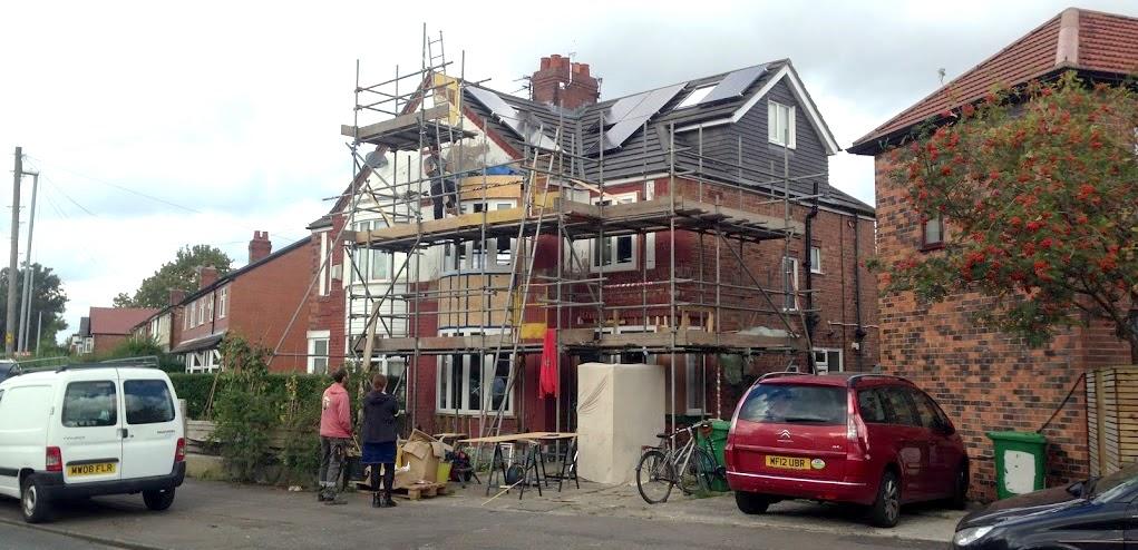 photo of a semi-detached house with scaffolding and solar panels with two people looking on.