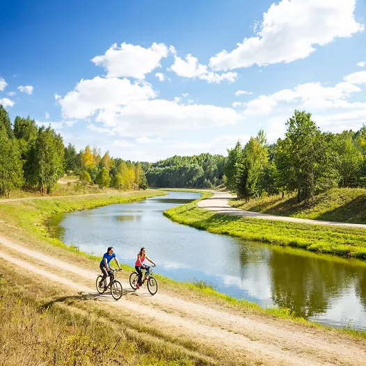 a photo of two people cycling alongside a riverbank in the sun